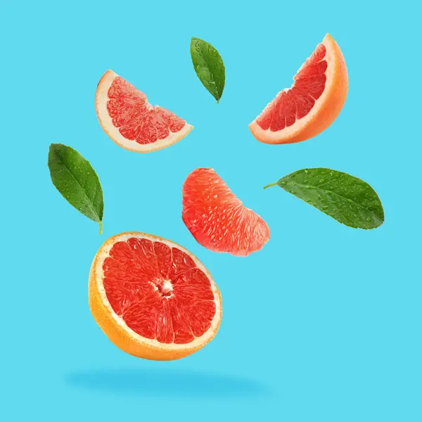 Pieces of grapefruit and green leaves falling on light blue background