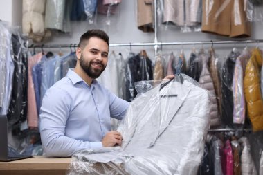 Kuru temizleme servisi. Kapalı mekanda naylon torba içinde askı tutan mutlu işçi.