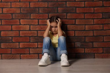 Çocuk istismarı. İçerideki tuğla duvarın yanında oturan üzgün küçük kız.