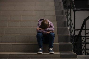 Çocuk istismarı. Evdeki merdivenlerde oturan üzgün çocuk.