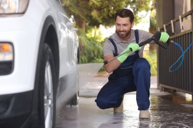 Worker washing auto with high pressure water jet at outdoor car wash