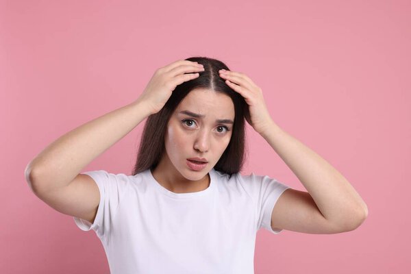 Грустная женщина осматривает волосы и кожу головы на розовом фоне. Проблема перхоти