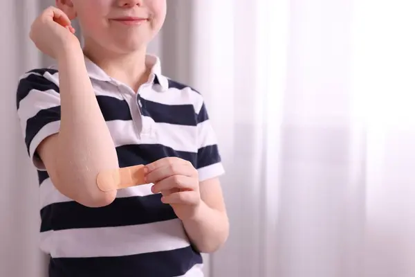 Little boy putting sticking plaster onto elbow indoors, closeup. Space for text
