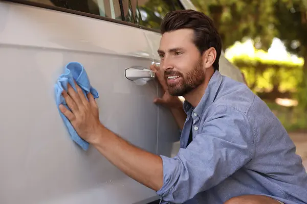Man cleaning car door with rag outdoors