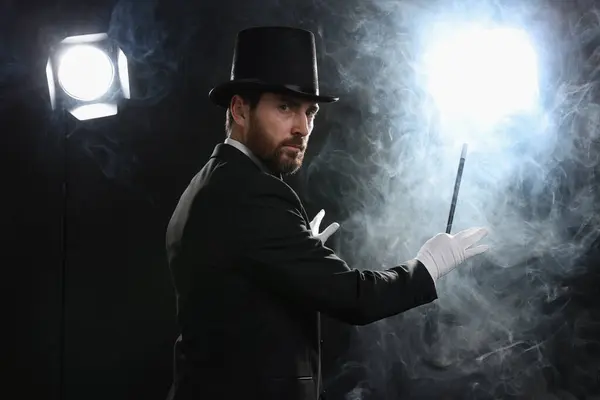 stock image Magician wearing top hat and holding wand in smoke on stage