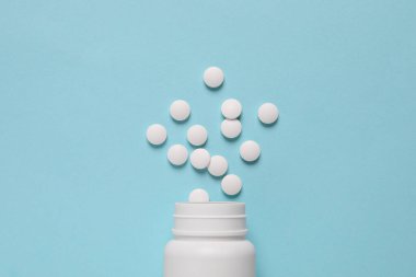 Açık mavi arka planda bir sürü beyaz haplı plastik şişe, düz yatıyordu.