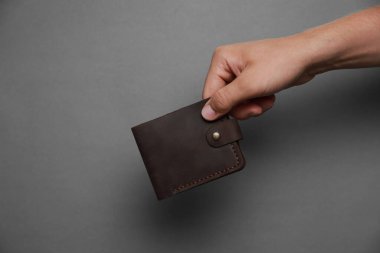 Koyu gri arka planda siyah deri cüzdan taşıyan adam, yakın plan. Metin için boşluk