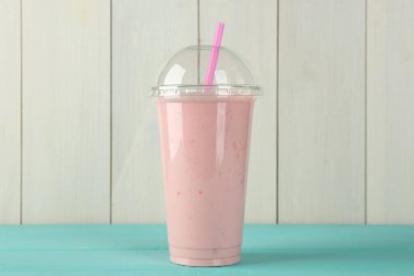 Beyaz ahşap duvara karşı açık mavi masada plastik bardaktaki lezzetli smoothie.