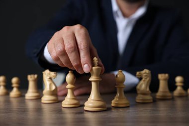 Ahşap masada satranç taşları olan adam karanlık arka plana karşı, yakın plan.