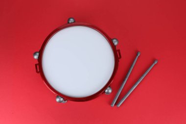 Drum and sticks on red background, top view. Percussion musical instrument clipart