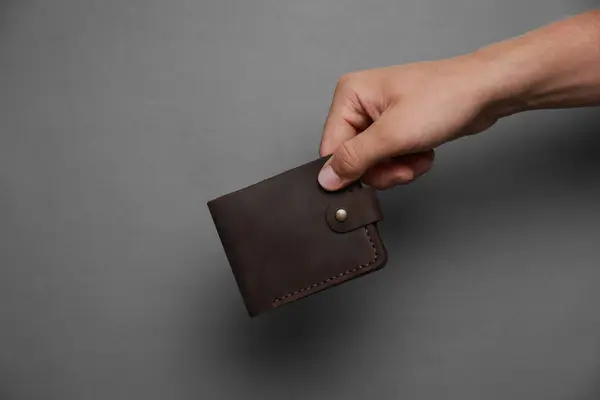 Man holding black leather wallet on dark grey background, closeup. Space for text