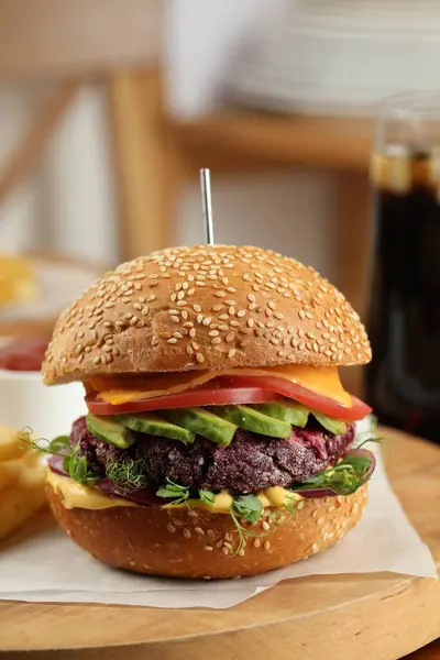 Tasty vegetarian burger with beet cutlet, cheese, avocado and tomato served on wooden table, closeup