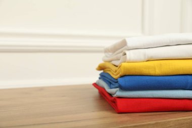 Sıralama ve düzenleme. Beyaz duvarın yanındaki ahşap masada yığınla farklı katlanmış kıyafet var. Metin için yeri olan yakın plan.