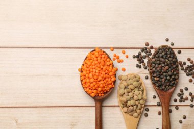 Açık ahşap masada farklı türde mercimeği olan kaşıklar. Metin için boşluk