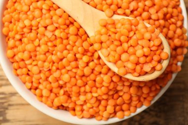 Tabakta çiğ kırmızı mercimek ve tahta masada kaşık, üst manzara.