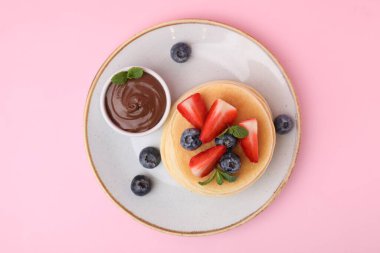 Çilekli, böğürtlenli, nane ve çikolata soslu lezzetli gözlemeler pembe arka planda, üst manzara