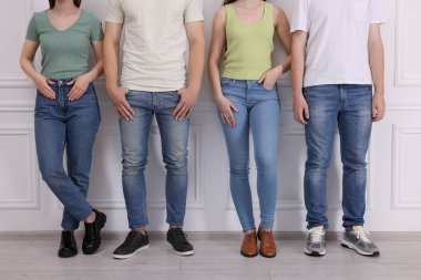 Beyaz duvarın yanında şık kotlu bir grup insan, yakın plan.