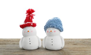 Beyaz arka planda, ahşap masada şapkalı sevimli kardan adamlar.