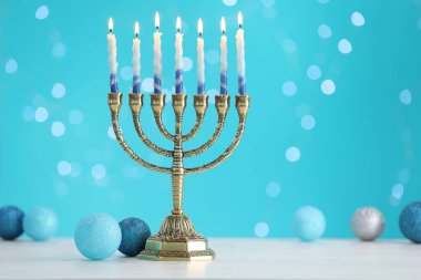 Hanukkah celebration. Menorah with burning candles and baubles on table against light blue background with blurred lights, space for text clipart