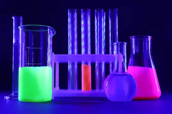 Laboratory glassware with luminous liquids on dark blue background