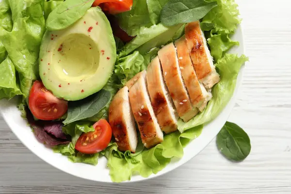 Delicious salad with chicken, cherry tomato and avocado on white wooden table, top view