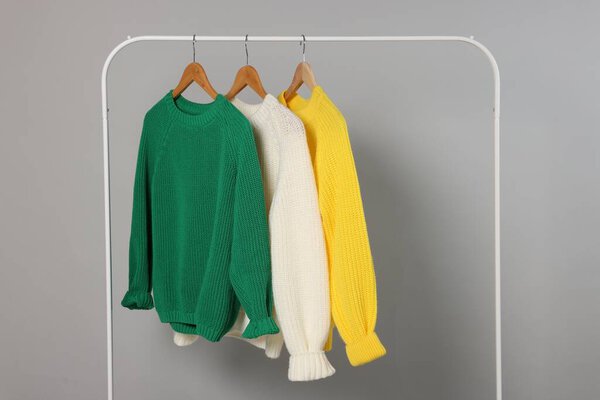 Rack with different warm sweaters on light grey background