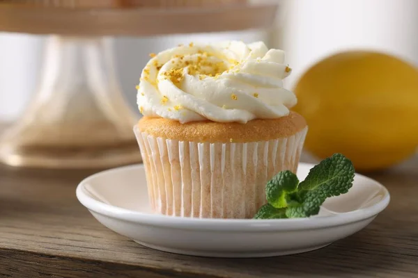 Delicious lemon cupcake with white cream and mint on wooden table, closeup