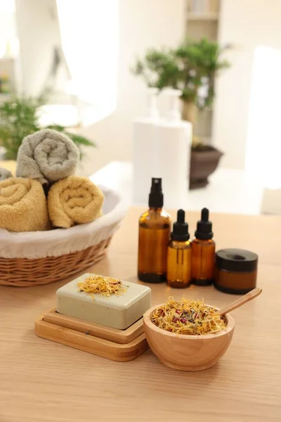Soap bar, dry flowers, bottles of essential oils, jar with cream and towels on wooden table indoors. Spa time