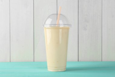 Beyaz ahşap duvara karşı açık mavi masada plastik bardaktaki lezzetli smoothie.