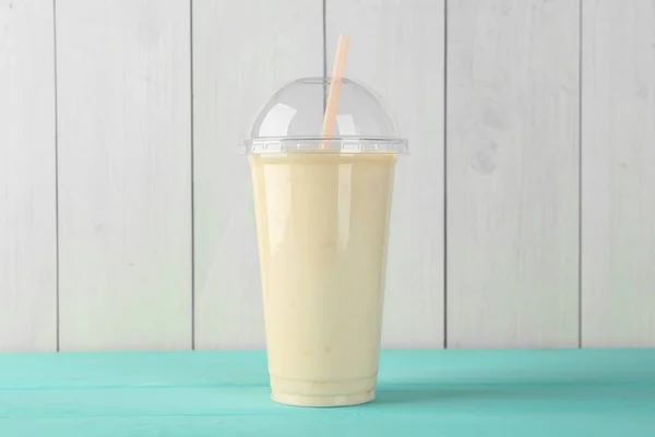 Tasty smoothie in plastic cup on light blue table against white wooden wall