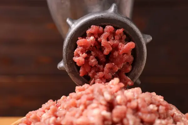 Manual meat grinder with beef mince against blurred background, closeup