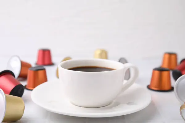 Cup of coffee and capsules on white table, closeup. Space for text