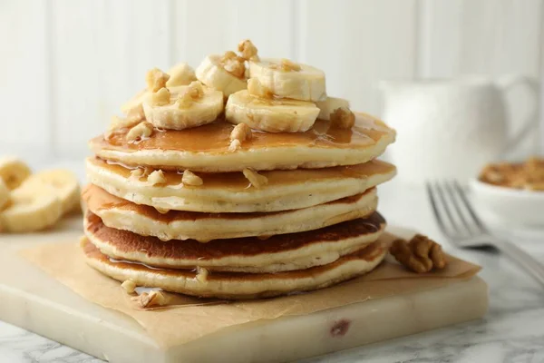Delicious pancakes with bananas, walnuts and honey on white marble table, closeup