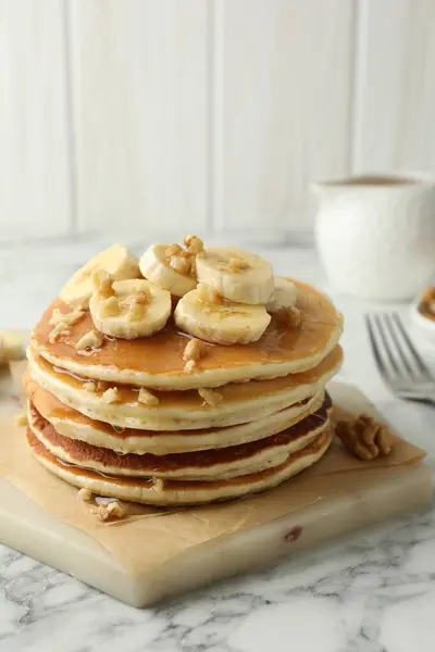 Delicious pancakes with bananas, walnuts and honey on white marble table