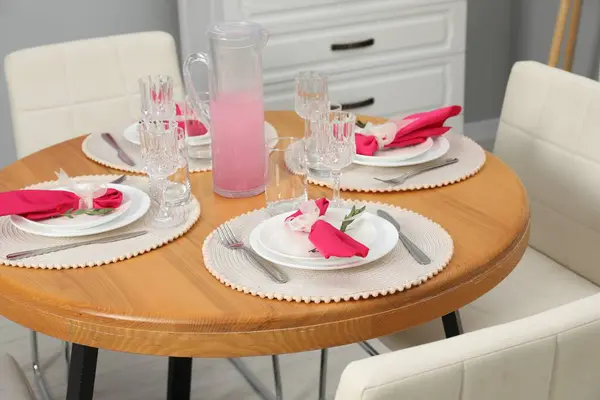 Color accent table setting. Glasses, plates, jug of beverage and pink napkins in dining room