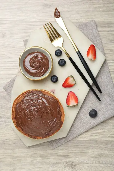 Delicious pancakes with chocolate paste, berries and cutlery on wooden table, top view