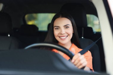 İyi yolculuklar. Arabasını kullanan mutlu genç bir kadın, ön camdan manzaralı.