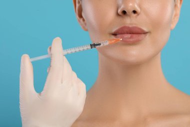 Doktor açık mavi arka planda genç bayana dudak iğnesi yapıyor, yakın plan. Estetik ameliyat