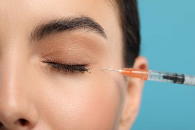 Açık mavi arka planda yüz enjeksiyonu yaptıran genç bir kadın, yakın plan. Estetik ameliyat