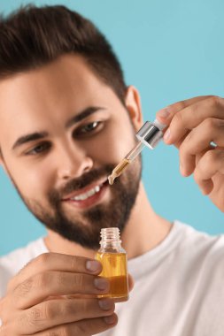 Elinde kozmetik serumu olan yakışıklı bir adam açık mavi arka planda, seçici odaklı.