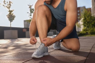 Güneşli bir günde dışarı çıkmadan önce ayakkabı bağcıklarını bağlayan adam, yakın çekim.