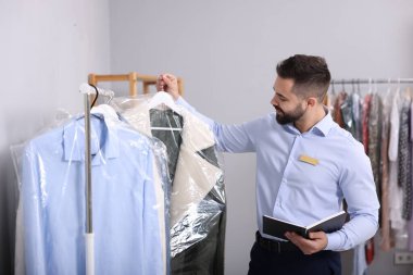 Kuru temizleme servisi. Kapalı mekanda plastik torba içinde askısı olan bir işçi.