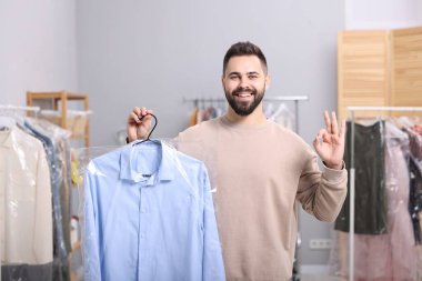 Kuru temizleme servisi. İçinde plastik torba olan askısı olan mutlu bir adam.