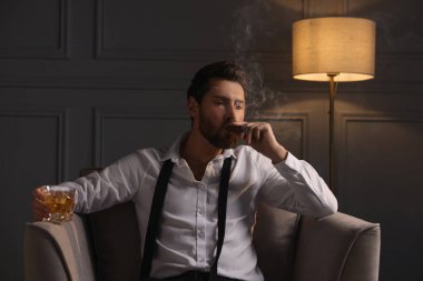 Evdeki koltukta puro içen yakışıklı bir adam.