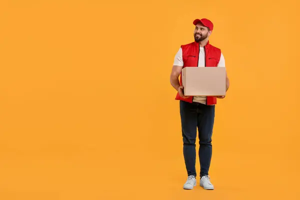 Happy young courier with parcel on orange background. Space for text