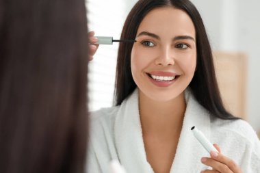 Güzel bir kadın kirpiklerine serum sürüyor, aynada yansıyor. Kozmetik ürünü