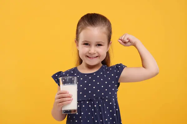 オレンジ色の背景に彼女の強さを示す新鮮なミルクのガラスとかわいい少女 — ストック写真