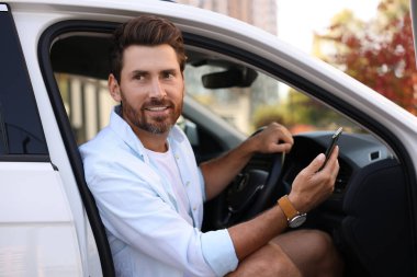 Akıllı telefonlu mutlu sakallı adam arabada oturuyor.