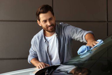 Gülümseyen adam arabanın ön camını temizliyor.