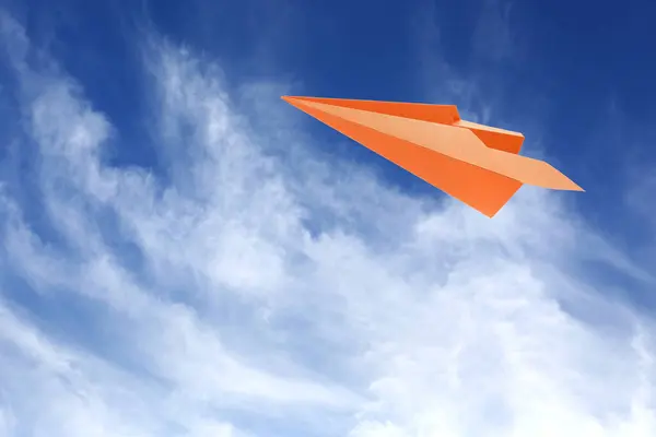 Orange paper plane flying in blue sky with clouds